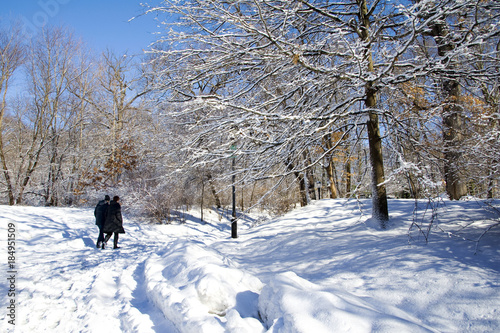 A couple walks through a snow trail during winter. Trees in background