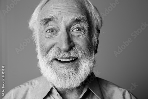 Sincere amazement. Close up black-and-white portrait of aged happy pensioner with widely open eyes while standing. Isolated on grey background