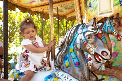 Happy female toddler ridding colorful carousel horse. © narstudio
