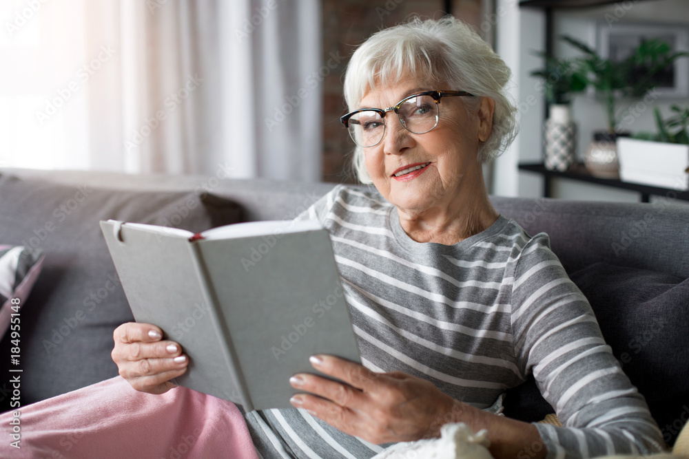 Portrait of mature woman resting at living room. She is reading novel and smiling Portrait of mature woman resting at living room. She is reading novel and smiling