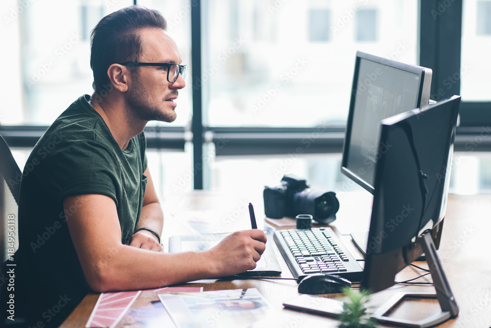 © Yakobchuk Olena - Side view orderly bearded retoucher working with graphic electronic tablet while situating at desk. Occupation concept