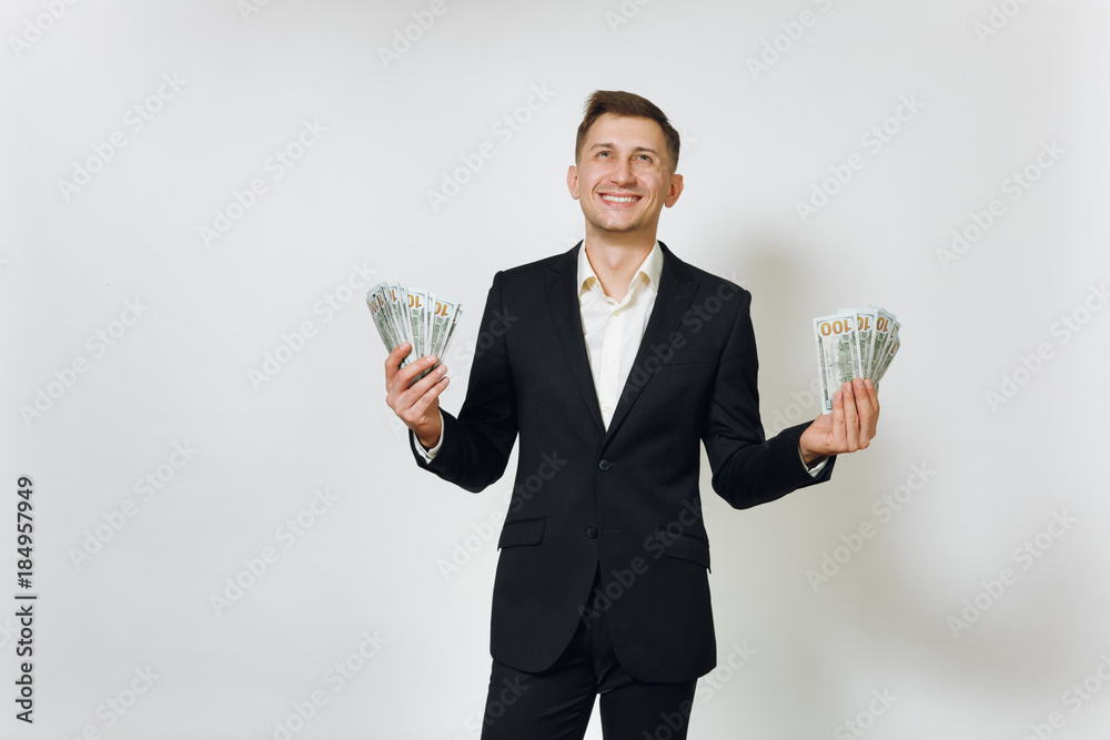 Young successful handsome rich business man in black suit holding wad of cash dollars isolated on white background for advertising. Concept of money, achievement, career and wealth in 25-30 years.