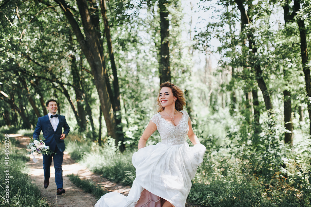 The bride and groom are happily running along the path in the forest. The bridegroom is catching up with the bride. The newlyweds laugh. The bride and groom are happily running along the path in the forest. The bridegroom is catching up with the bride. The newlyweds laugh.