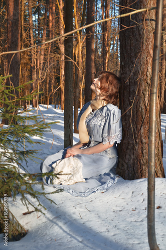 girl in blue dress sitting on the snow in the woods