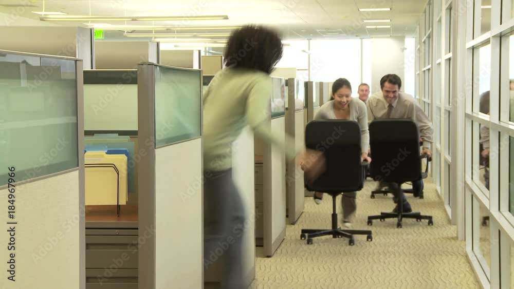 Young business colleagues racing with chairs in office Young business colleagues racing with chairs in office