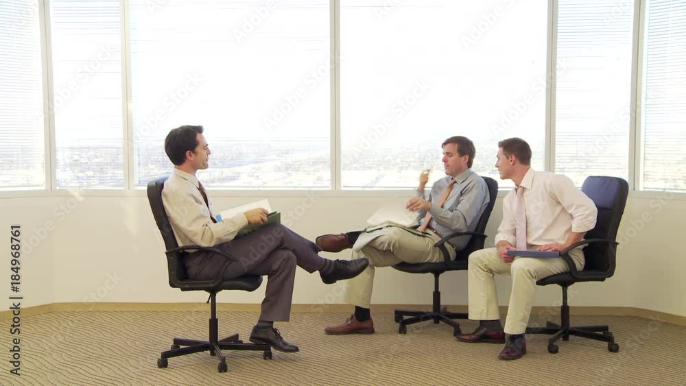 Three businessmen sitting in office chairs while talking Three businessmen sitting in office chairs while talking