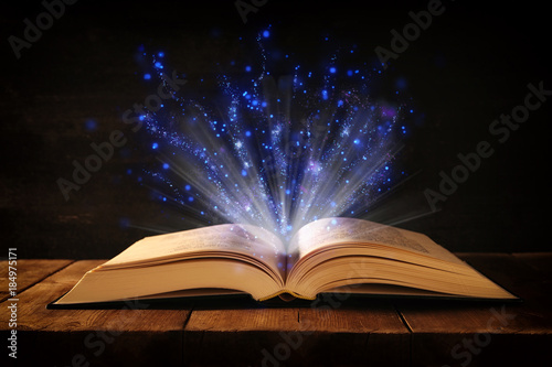 image of open antique book on wooden table with glitter overlay.
