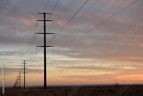 Long row of electricity pylons and power lines fading into the distant horizon at sunset in a rural setting