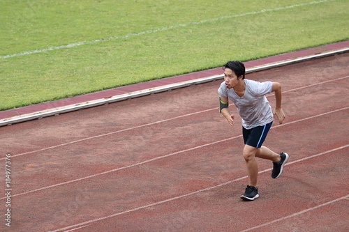 Handsome athlete Asian man running on racetrack in stadium with copy space background. Healthy active lifestyle concept. © tuaindeed