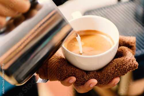 Barista pouring milk into a cup of coffee for making latte coffee in the coffee shop