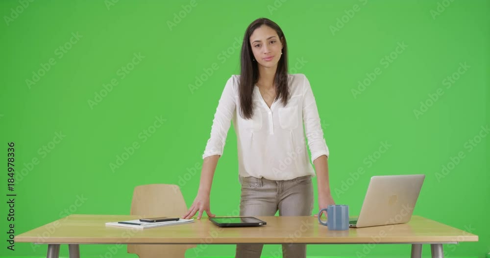 A Hispanic woman stands at her desk looking at the camera on green screen. On green screen to be keyed or composited. A Hispanic woman stands at her desk looking at the camera on green screen. On green screen to be keyed or composited.