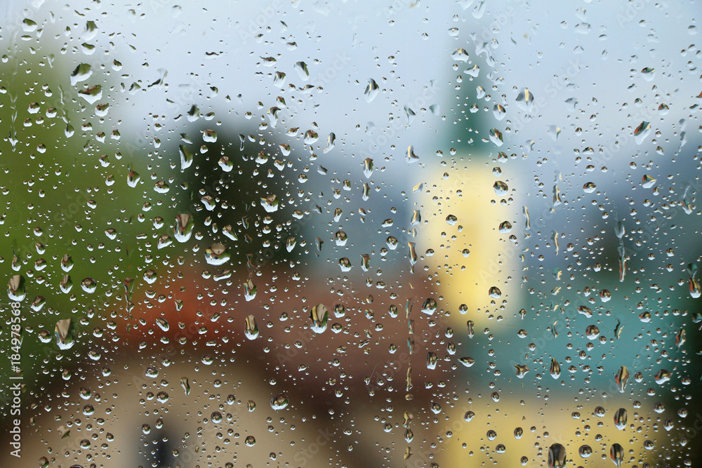 Rain drops on window glass with house and church in background Rain drops on window glass with house and church in background