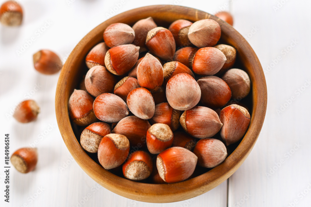 Hazelnut nuts in a wooden bowl on a white wooden table. Superfood. Hazelnut nuts in a wooden bowl on a white wooden table. Superfood.