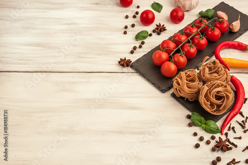 Macaroni in the form of nests on a white wooden background with tomatoes and various spices