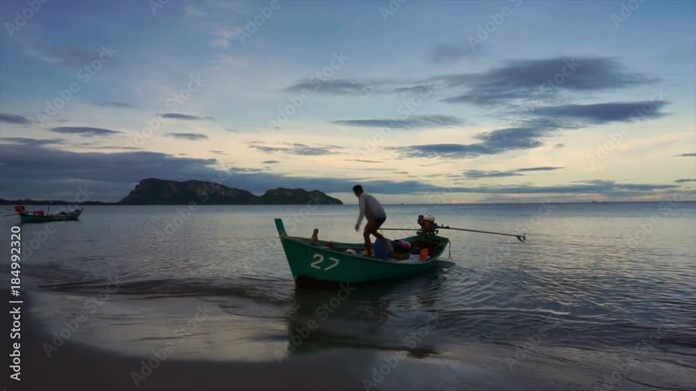 PrajuabKirikhan,Thailand.September 26,2017. asian fisherman is on the green boat and trying to start the engine at dusk. life, nature concept. PrajuabKirikhan,Thailand.September 26,2017. asian fisherman is on the green boat and trying to start the engine at dusk. life, nature concept.