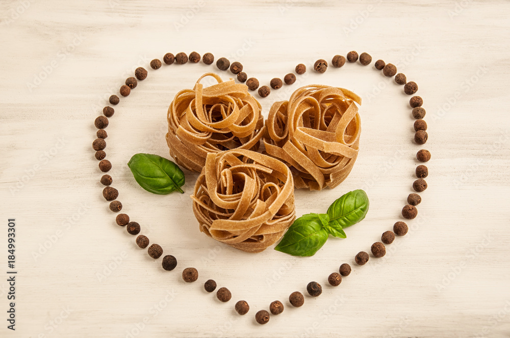 Macaroni in the form of nests with basil in the shape of heart on a white wooden background Macaroni in the form of nests with basil in the shape of heart on a white wooden background
