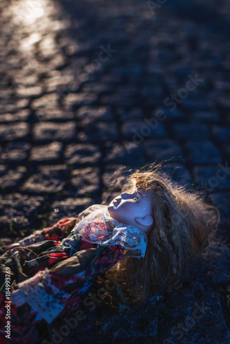 Vintage china doll lying in cobblestone street backlit by low autumn sunlight.