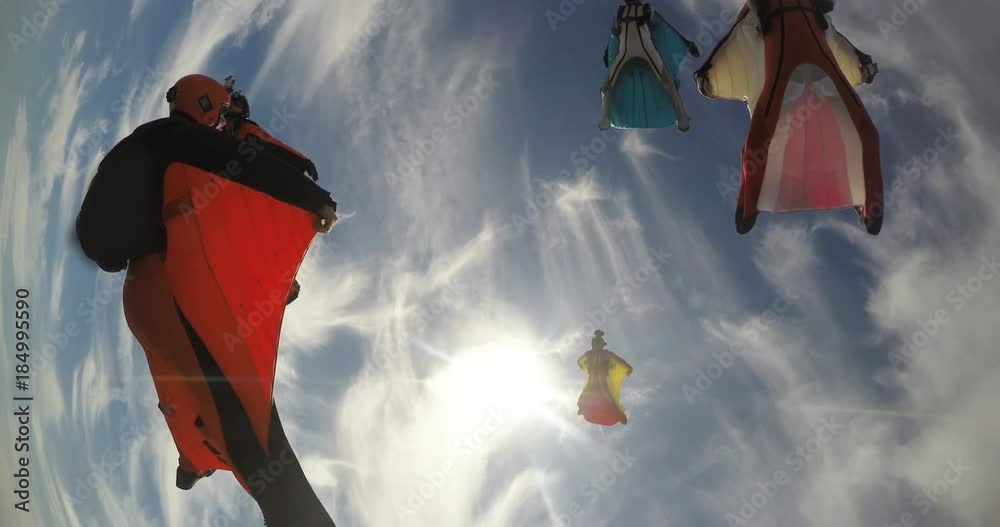 A base jumper in a wingsuit leaping off a from a rocky cliff, gliding down over a green landscape