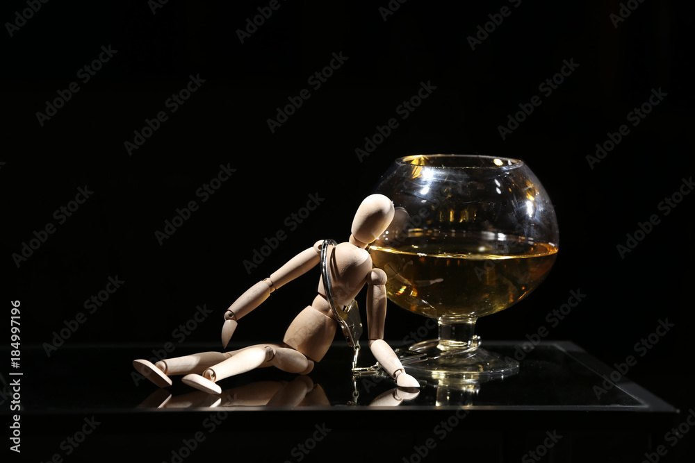 Composition of doll, alcohol and handcuffs against dark background. Concept of bad habits