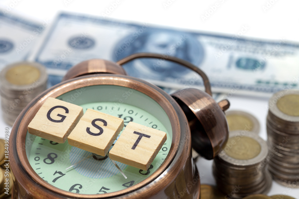Goods and Services Tax word on Alarm clock and stacks coins on white table, Success in business concept. Goods and Services Tax word on Alarm clock and stacks coins on white table, Success in business concept.