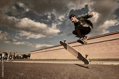 Фотография Freeze action shot of talented skillful young European male skateboarder jumping high while performing kick flip trick on his wooden long board on sunny summer day