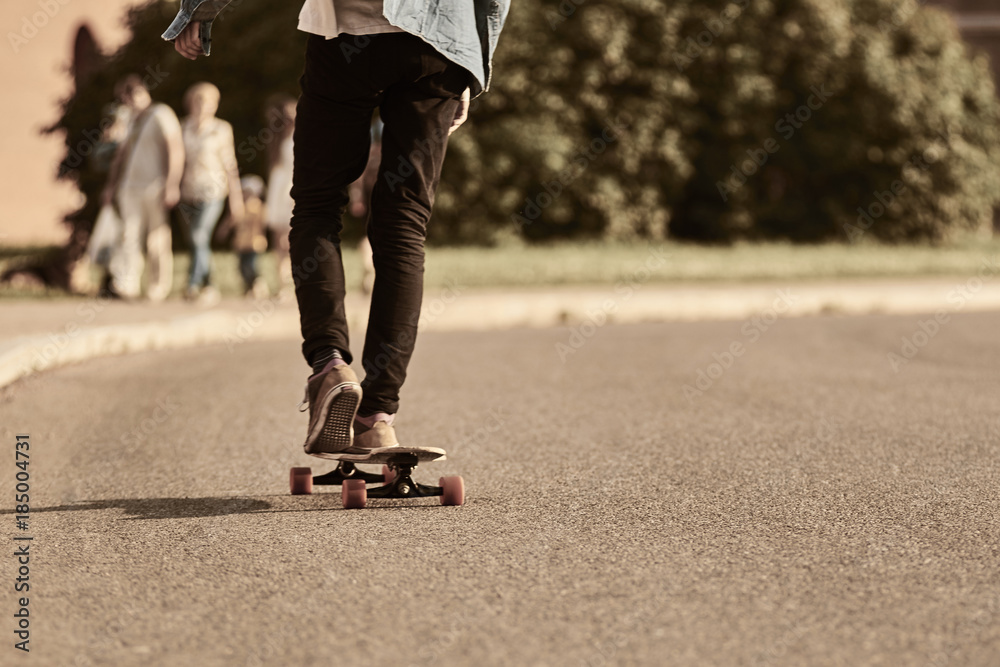 Rear view of unrecognizable teenage boy wearing shabby kicks and black  skinny jeans commuting to school using longboard. Cropped view of stylish  hipster guy riding skateboard down empty road Stock-Foto | Adobe