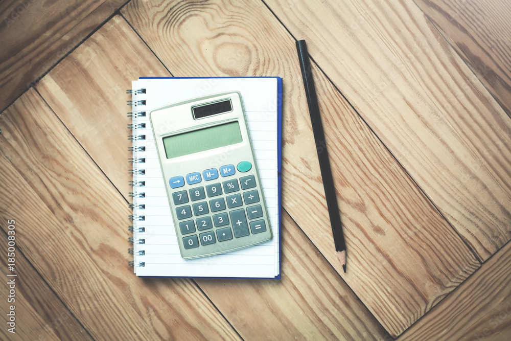 Calculator with notepad and black pencil on a wood background. Calculator with notepad and black pencil on a wood background.