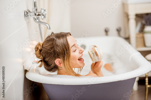 Young woman singing with brush relaxing in the beautiful vintage bath full of foam in the bathroom