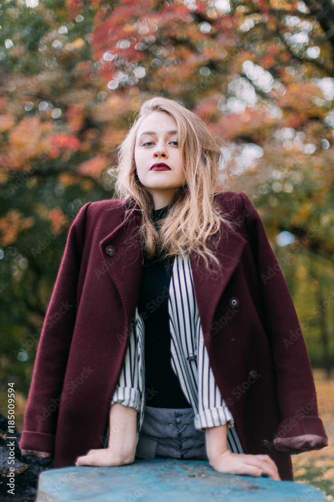 portrait of a luxurious, beautiful, young girl. Dressed in stylish clothes, walking in an autumn park. Bright lipstick on the lips.