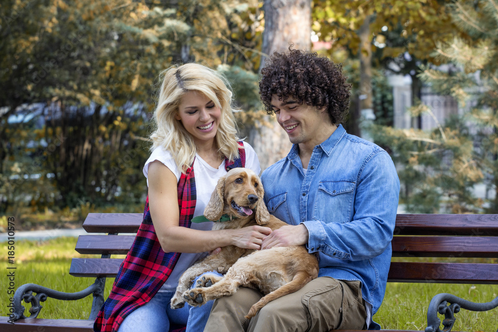 Young couple sitting at the bench in the park with his dog