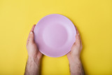 Empty ceramic round plate in man's hands isolated on yellow background