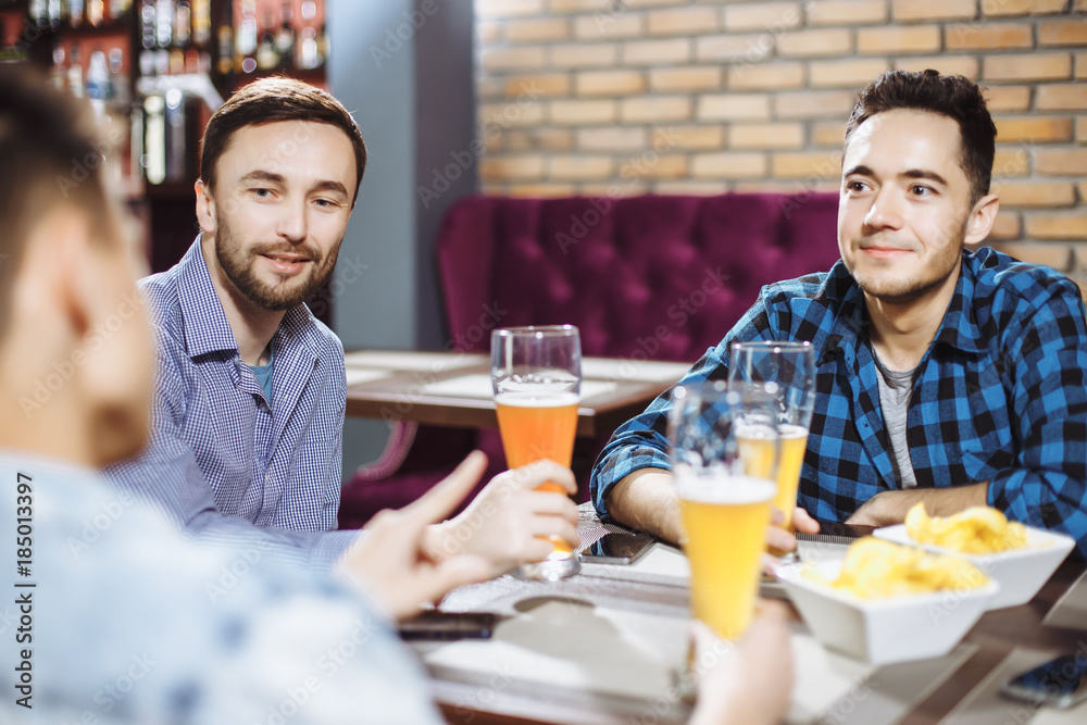 People, men, leisure, friendship and celebration concept - happy male friends talking and drinking beer at bar or pub.
