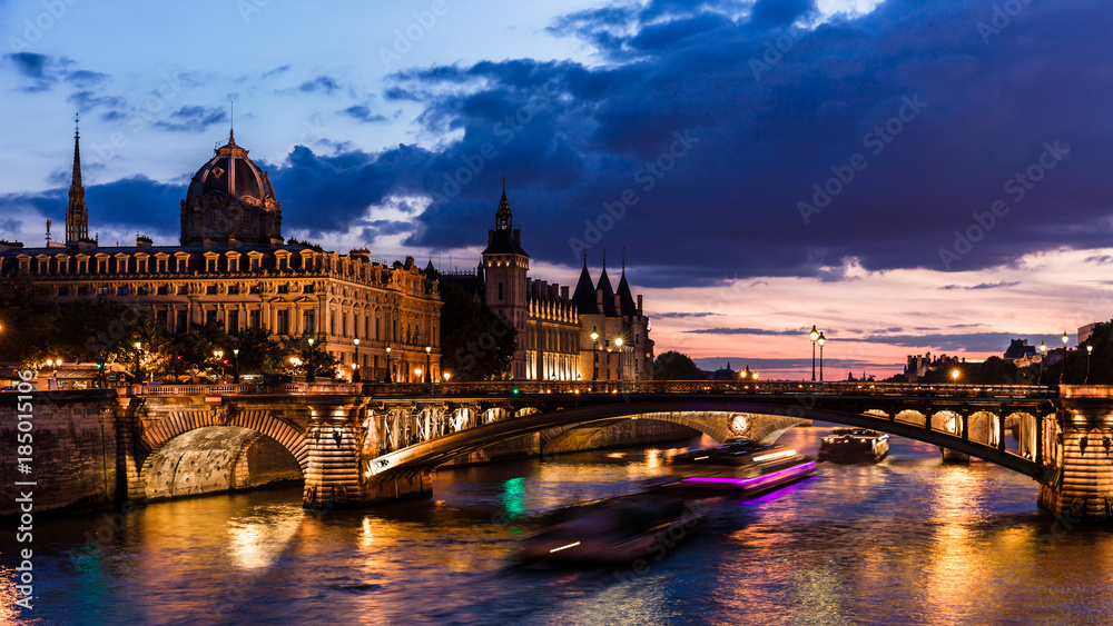 Night view of Conciergerie Castle and Pont Notre-Dame bridge over river Seine. Paris, France