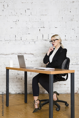 Young blond beauty businesswoman sitting at a office table with laptop, notebook and glasses in suit. Business concept. photo