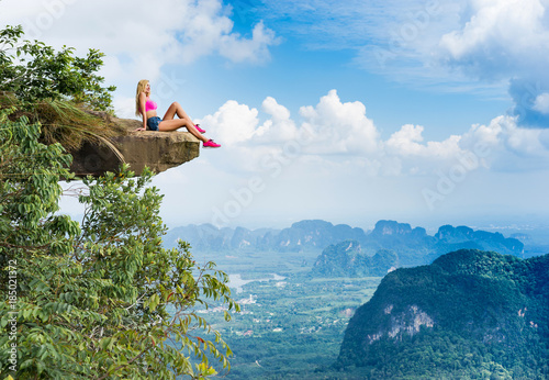 Happy young girl sitting on the top of mountain with a breathtaking view of the landscape with valley and rocks.