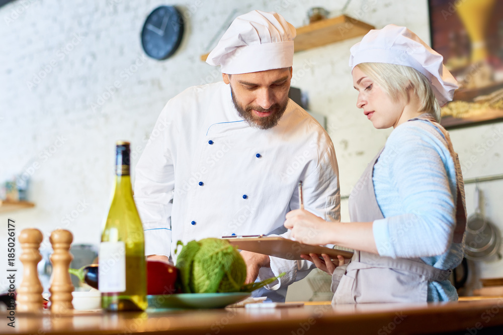 Portrait of mature chef and his apprentice cooking together in kitchen of modern restaurant, copy space Portrait of mature chef and his apprentice cooking together in kitchen of modern restaurant, copy space
