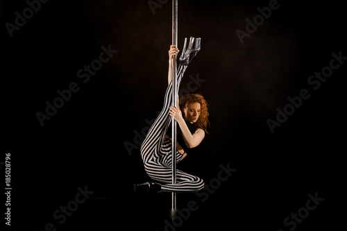 Young sexy woman exercises pole dance against a black background