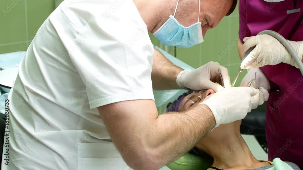 A dentist with an assistant removes the tooth from a young woman A dentist with an assistant removes the tooth from a young woman