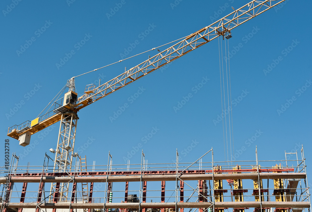 Eine Rohbau wächst unter einem Kranausleger und unter blauem Himmel in die Höhe Eine Rohbau wächst unter einem Kranausleger und unter blauem Himmel in die Höhe