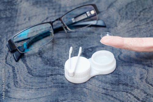 the girl on the background of the containers for storing contact lenses and glasses holds a contact lens on the finger