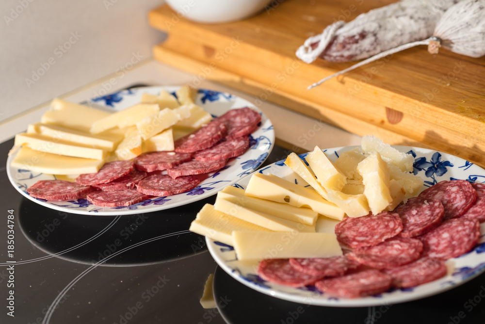 Platos listos para servir con un aperitivo consistente en trozos de queso y salchichón cortado en rodajas, escena en una cocina doméstica.