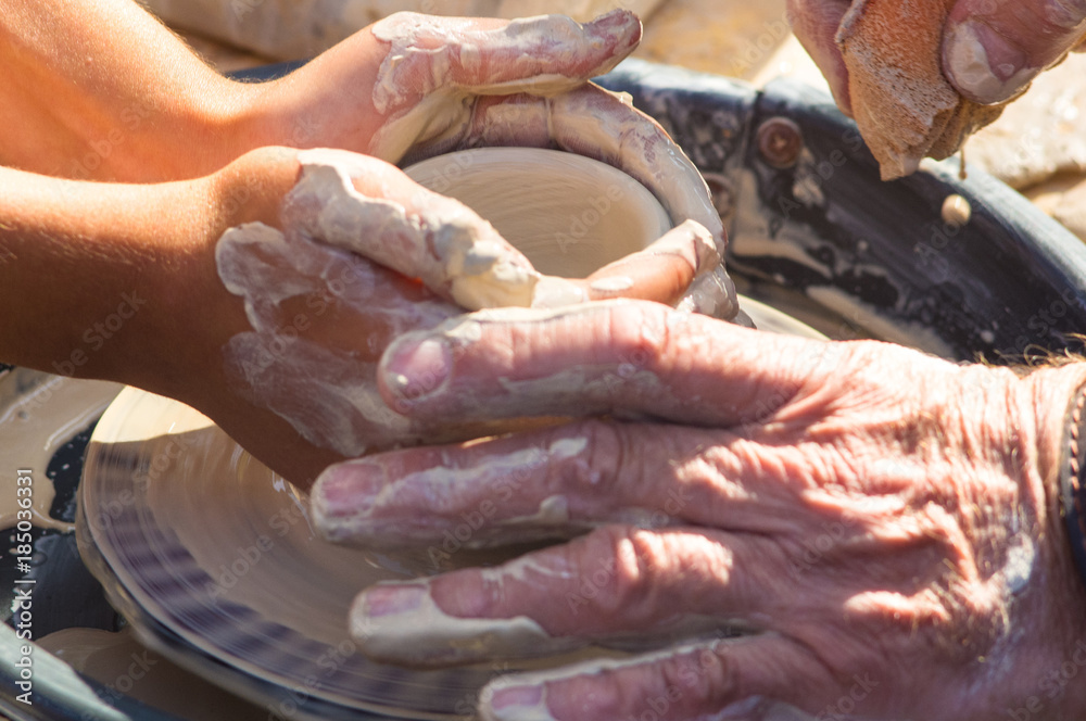 adult hand fed baby's hands to work with a potter's wheel
