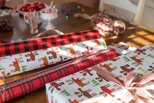 closeup of rolls of Christmas wrapping paper ribbon and gift on table at home in sunlight
