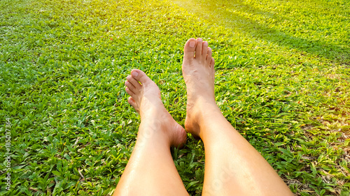 Woman leg lying on green meadow in sunset light time for barefoot relaxing concept.