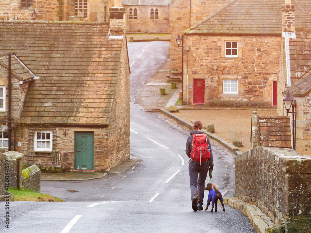 A hiker and their dog out walking through the village of Blanchland England, UK.
