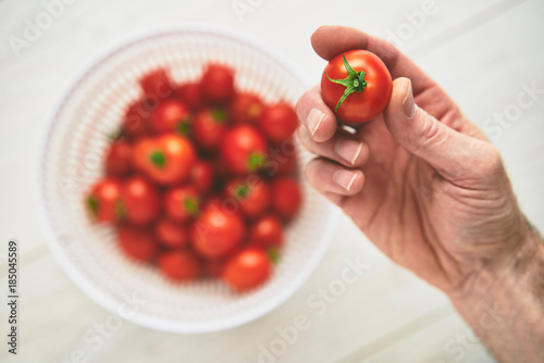 A mans hand picking up a fresh ripe red tomato on a pale wood wo