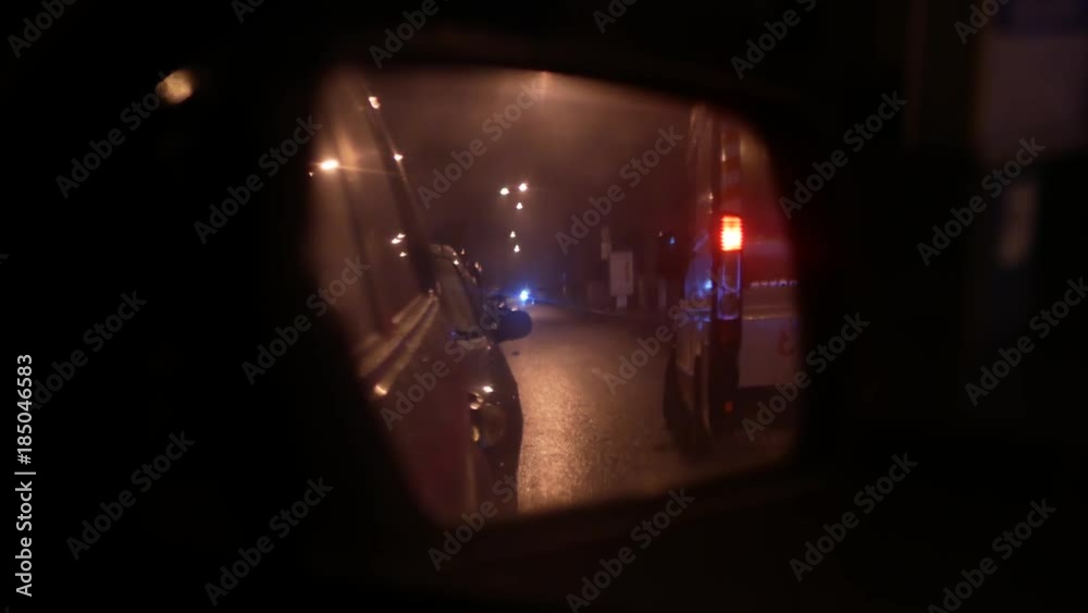 Wet car rear view mirror. Nighttime urban traffic. Ambulance car at the mirrror Wet car rear view mirror. Nighttime urban traffic. Ambulance car at the mirrror