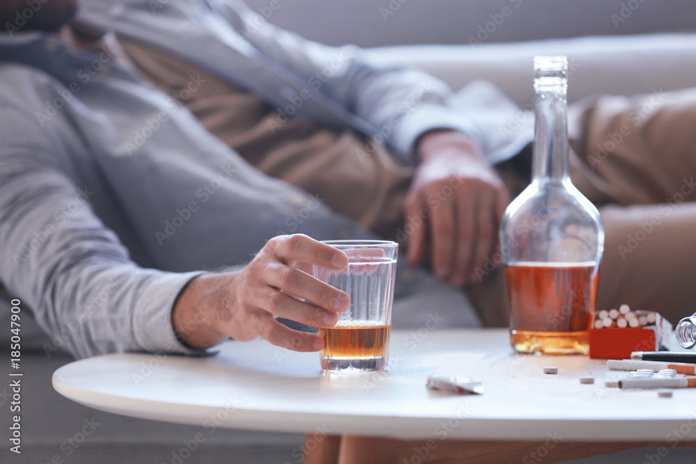 Drunk man lying on sofa with glass of whiskey in hand. Alcoholism concept Drunk man lying on sofa with glass of whiskey in hand. Alcoholism concept