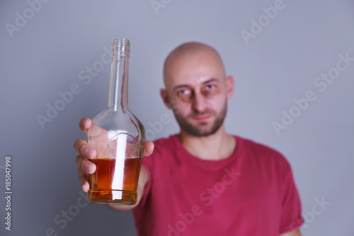 Drunk man with whiskey bottle on grey background. Alcoholism concept