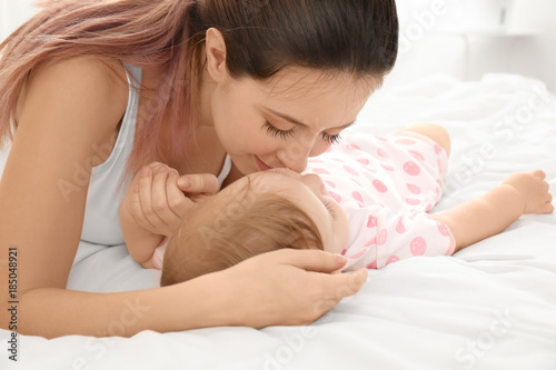 Young mother kissing her cute baby on bed